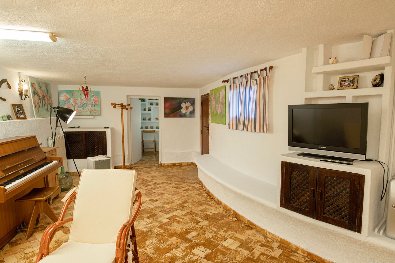 Salón rústico con suelos de barro cocido, piano de madera, mobiliario de obra integrado y paredes blancas de estilo mediterráneo tradicional.