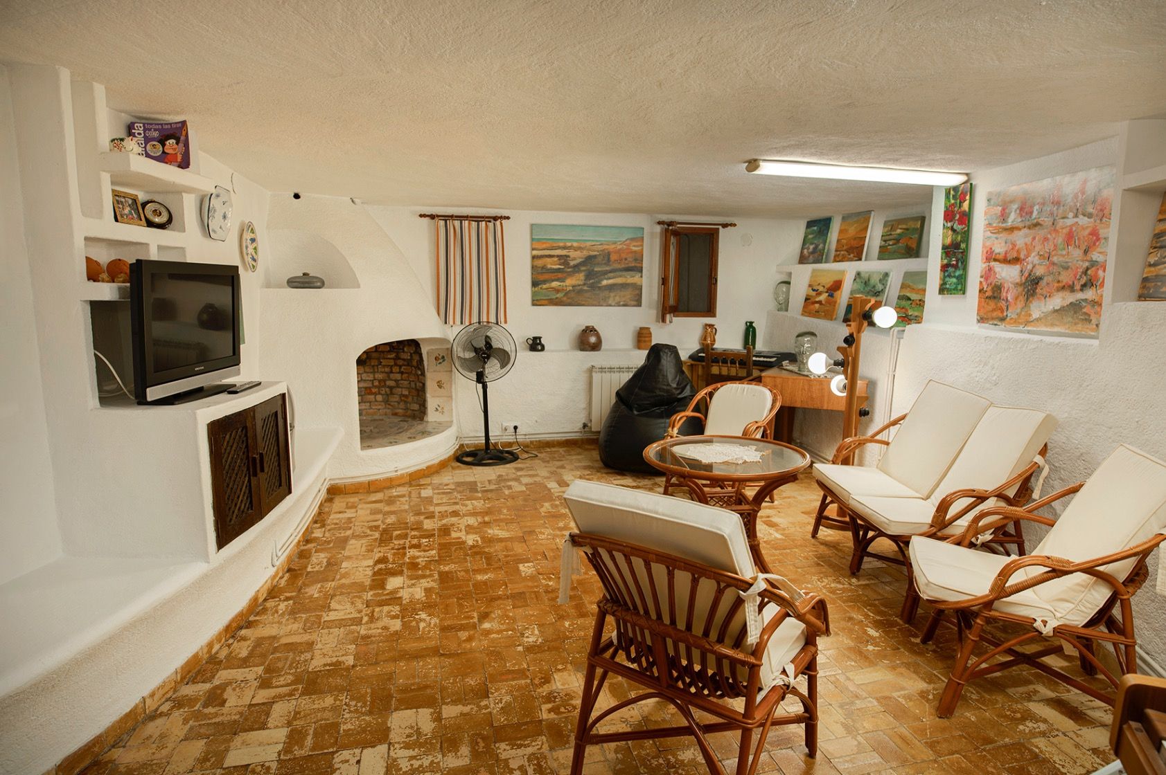 Salón rústico con suelos de terracota, chimenea de obra y paredes encaladas. Incluye mobiliario de bambú y una zona dedicada al arte con luz natural.