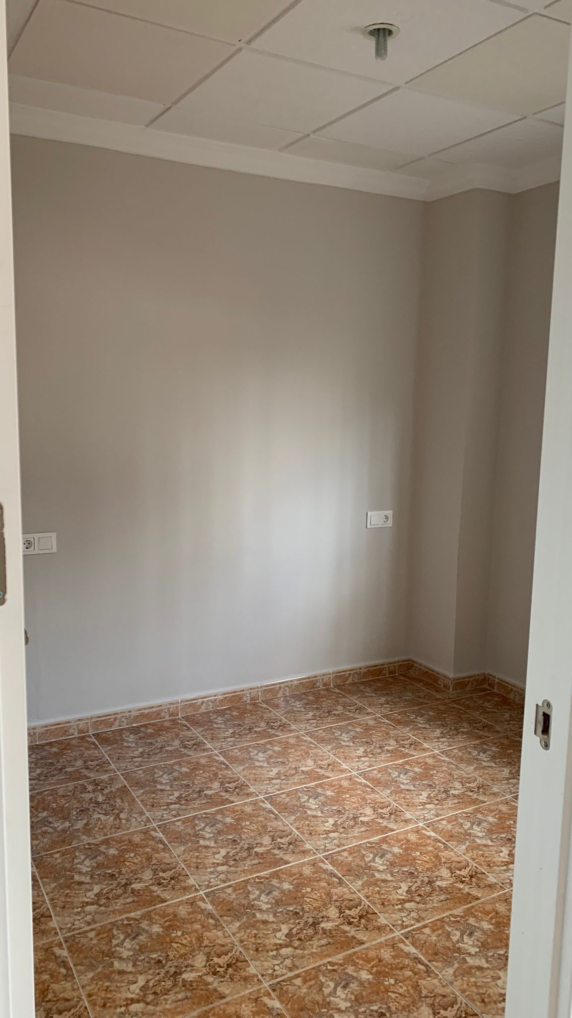 Habitación reformada con suelos de gres cerámico marmoleado, paredes en gris suave y techo modular con molduras blancas perimetrales.
