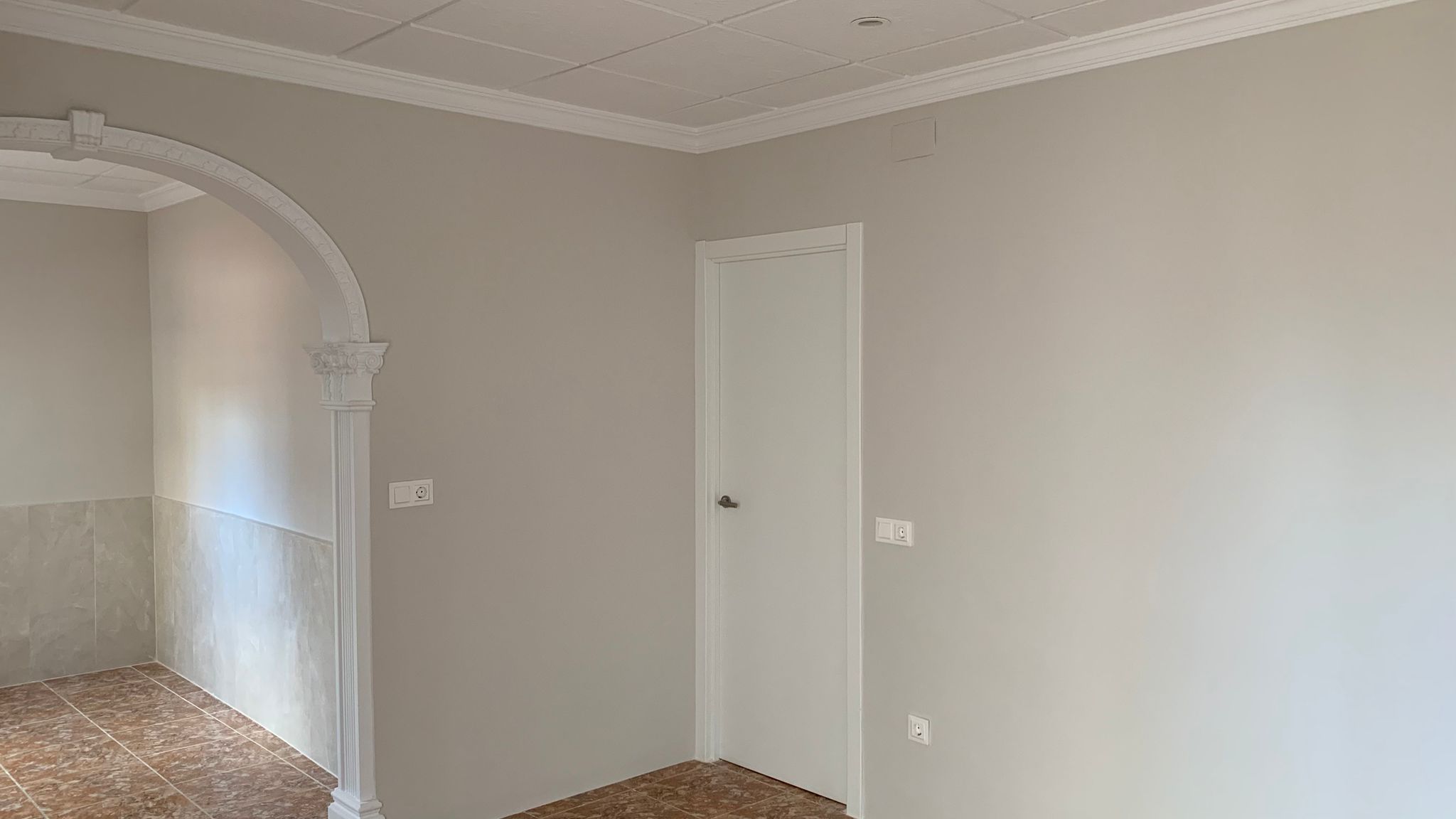 Interior reformado con un arco decorativo de estilo clásico, paredes en tonos neutros, suelos cerámicos y techos con molduras e iluminación empotrada.