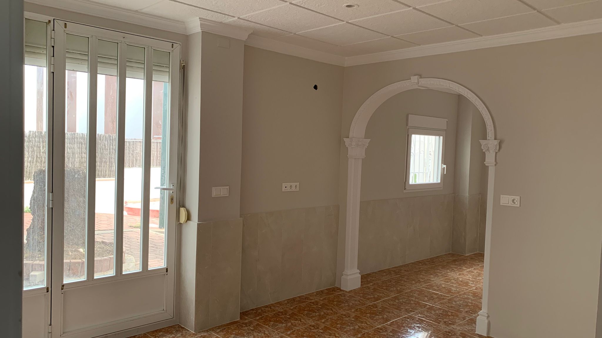 Salón con acceso directo al patio exterior, suelos de gres y un arco decorativo blanco que comunica los espacios de la planta baja reformada.