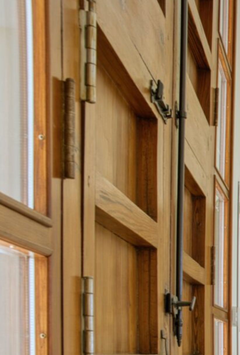 Detalle de carpintería de madera maciza con herrajes tradicionales y cierre de falleba vertical, integrando paneles de cristal para la entrada de luz.