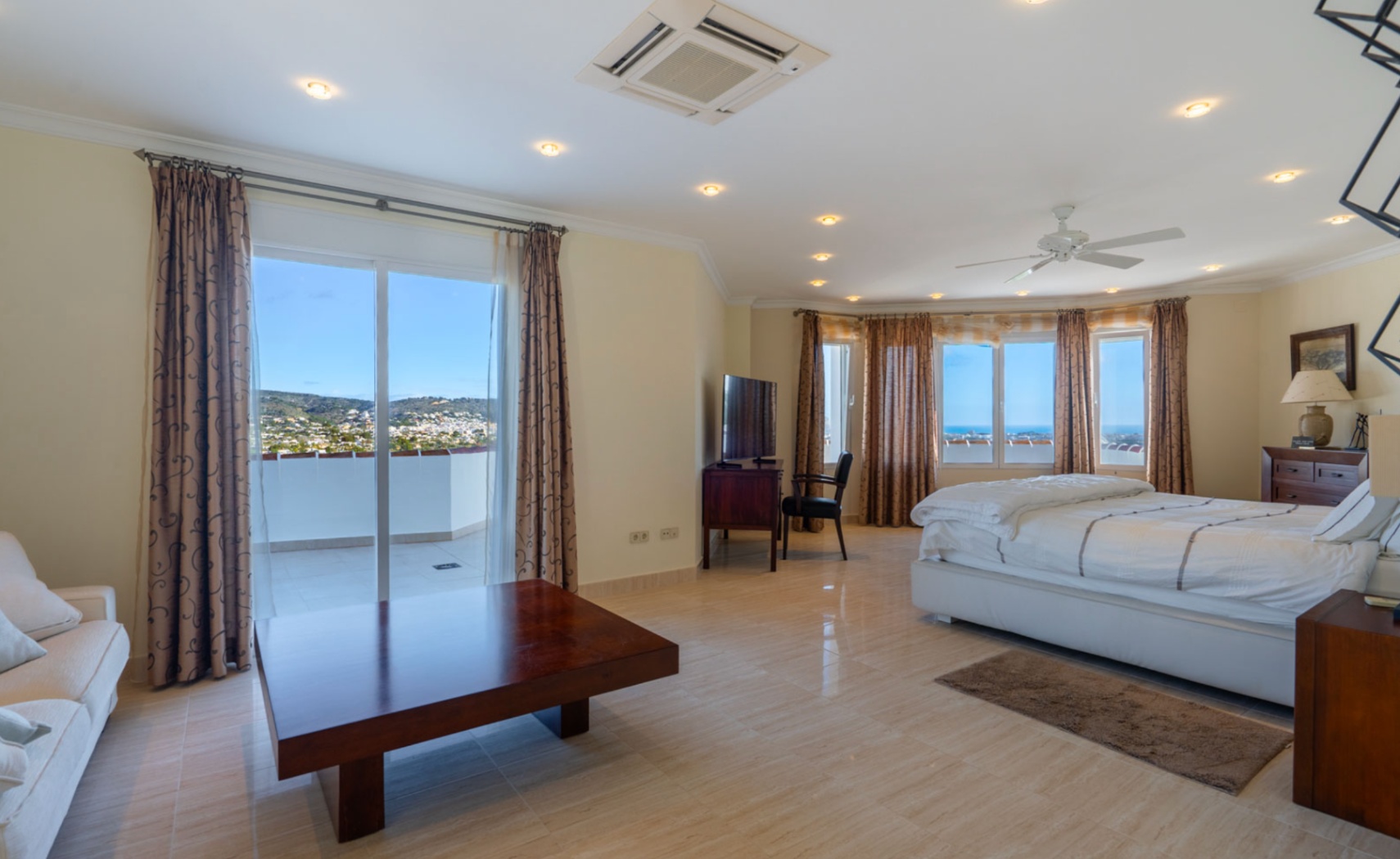 Dormitorio principal con acceso a terraza privada, suelos de gres pulido y vistas panorámicas al mar. Dispone de aire acondicionado, ventilador de techo e iluminación empotrada.