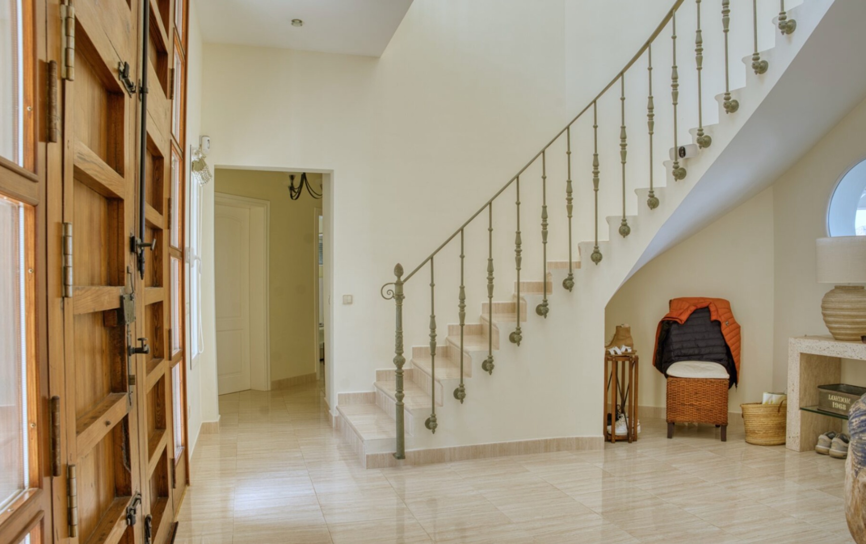 Hall de entrada con gran puerta de madera maciza y cristal. Destaca la escalera curva con barandilla de hierro forjado y suelos de mármol pulido.