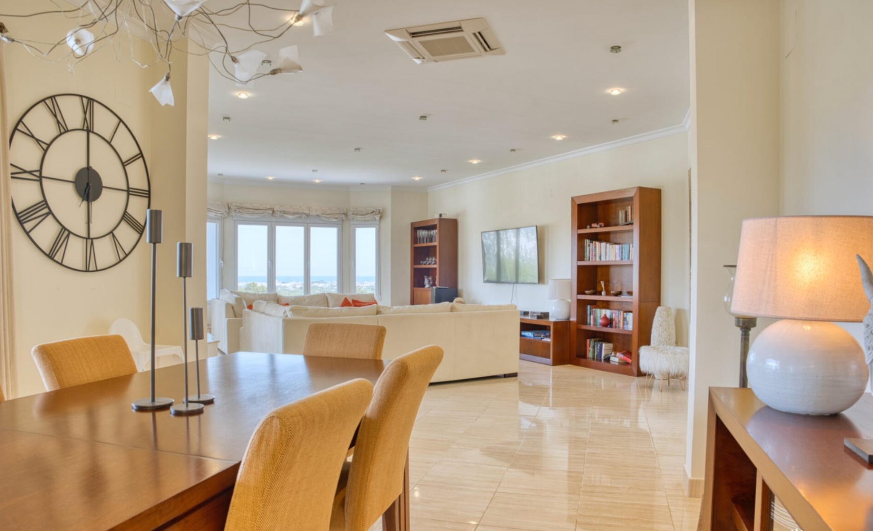 Salón-comedor diáfano con suelos de mármol pulido, mobiliario de madera y amplios ventanales que ofrecen vistas despejadas al mar Mediterráneo.
