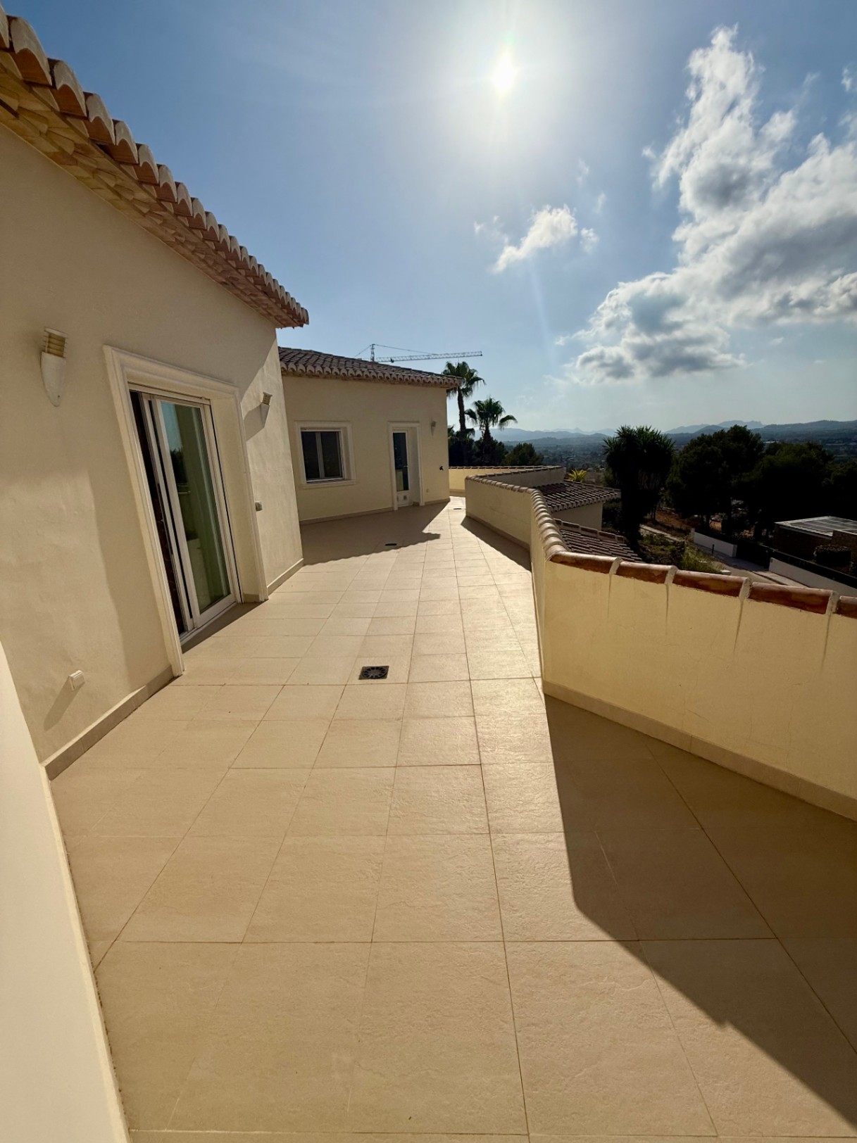 Terraza superior con pavimentos cerámicos en tonos crema y murete perimetral, ofreciendo vistas despejadas hacia el valle y las montañas bajo el sol mediterráneo.