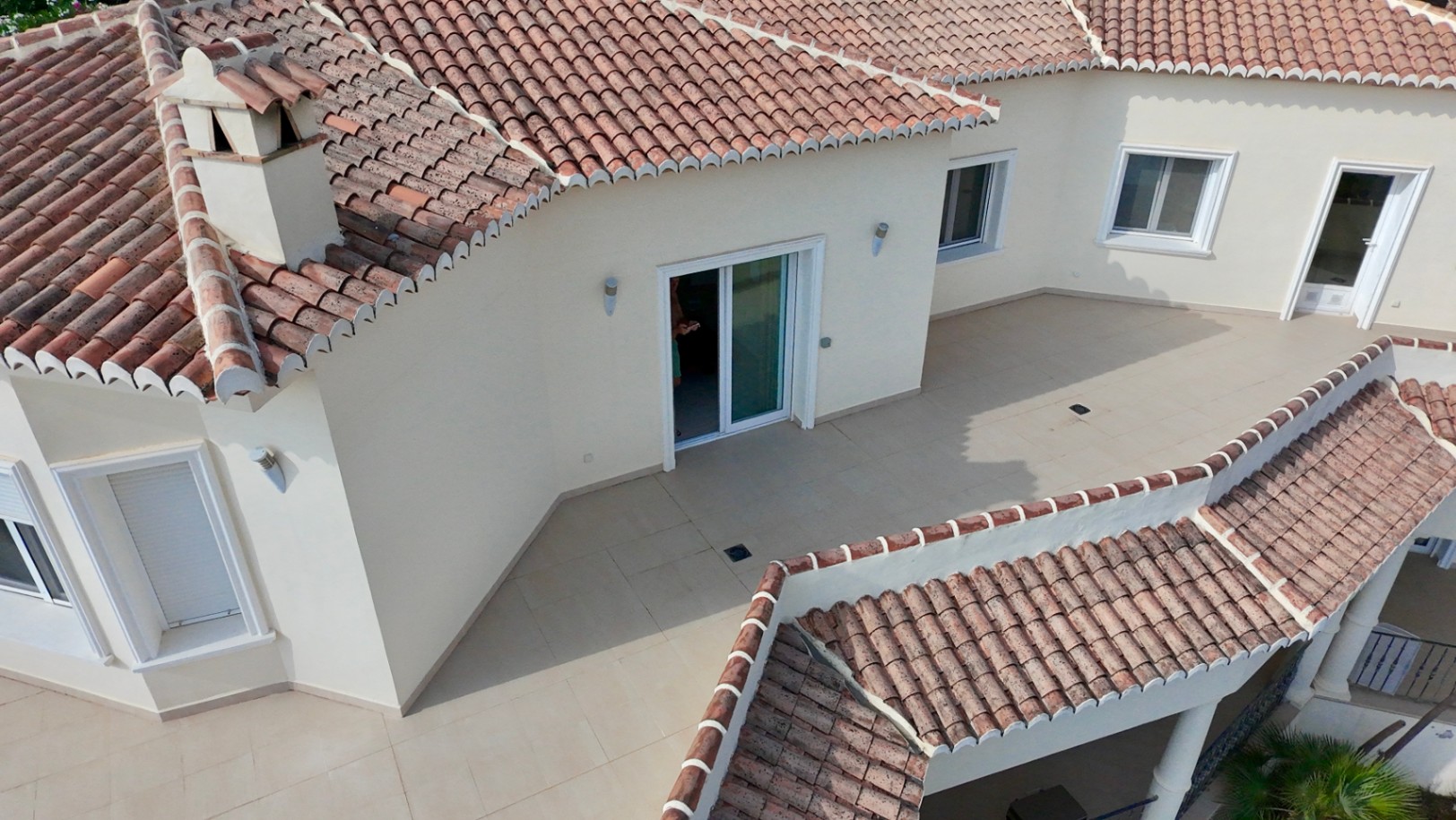 Vista aérea de la terraza superior y la arquitectura del tejado con teja curva tradicional, destacando la carpintería blanca y el suelo cerámico en tonos crema.