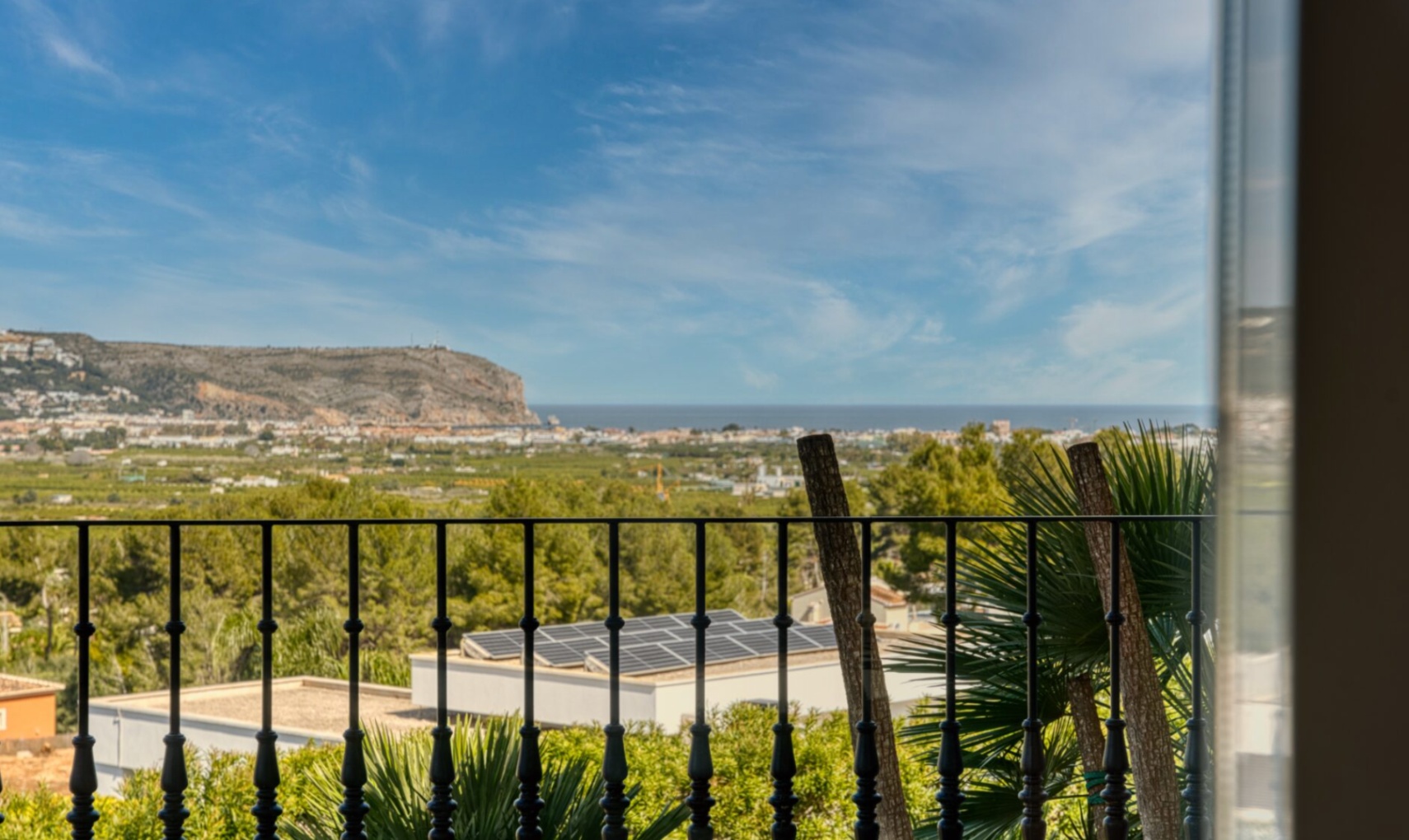 Vista panorámica desde la terraza con barandilla de hierro forjado, capturando el mar Mediterráneo y el cabo de San Antonio bajo un cielo despejado.